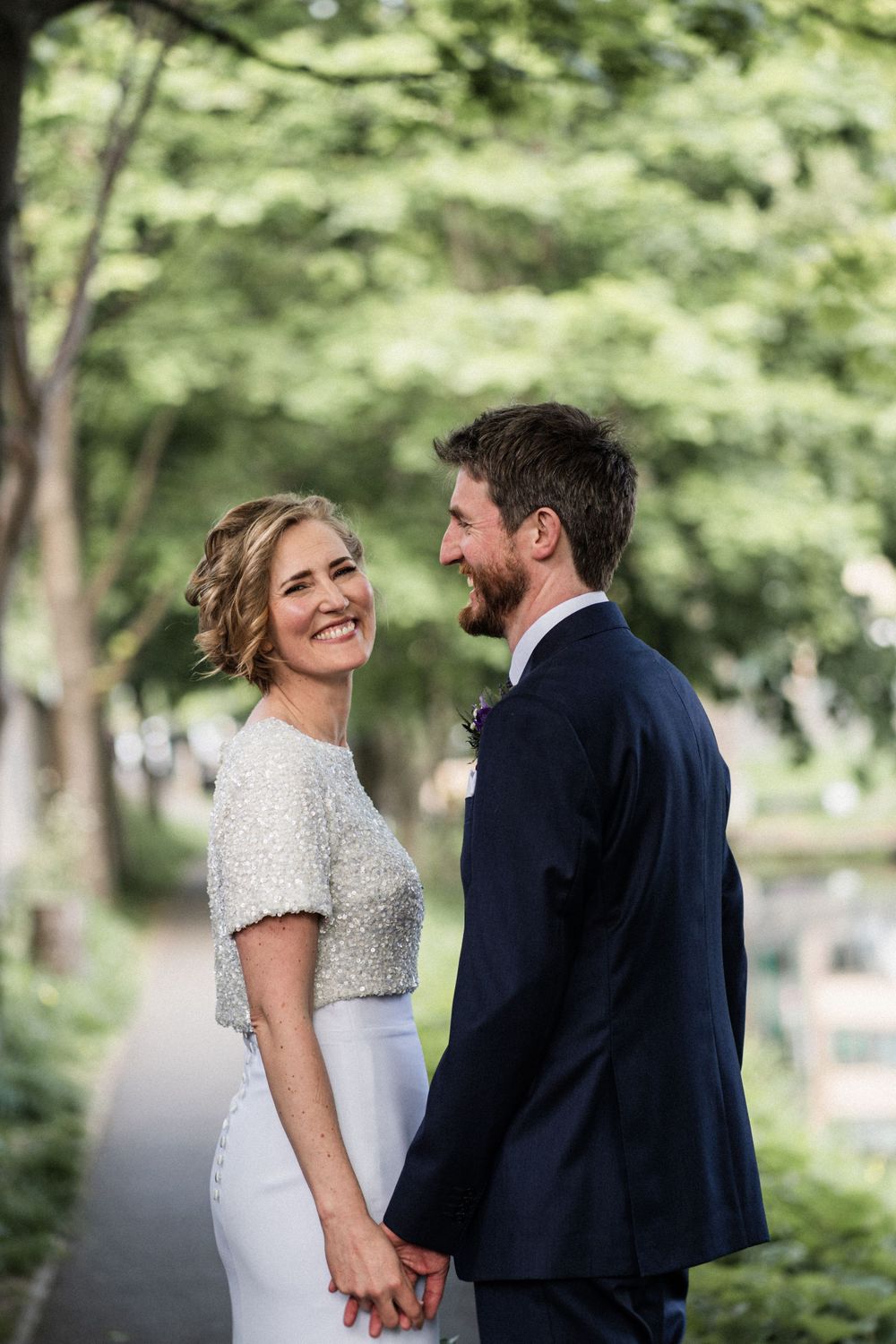 A newlywed couple share a romantic moment on a tree-lined path during their wedding day.