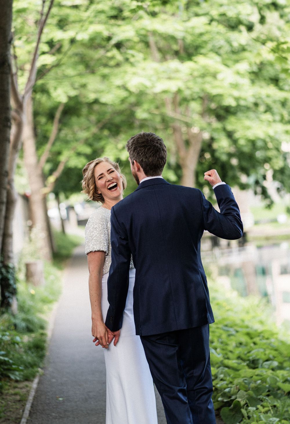 A joyful wedding moment captured as the couple laugh together on a garden path.