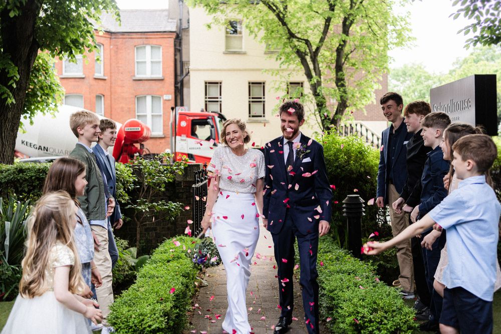A wedding couple walks through a garden path while guests shower them with confetti on their special day.