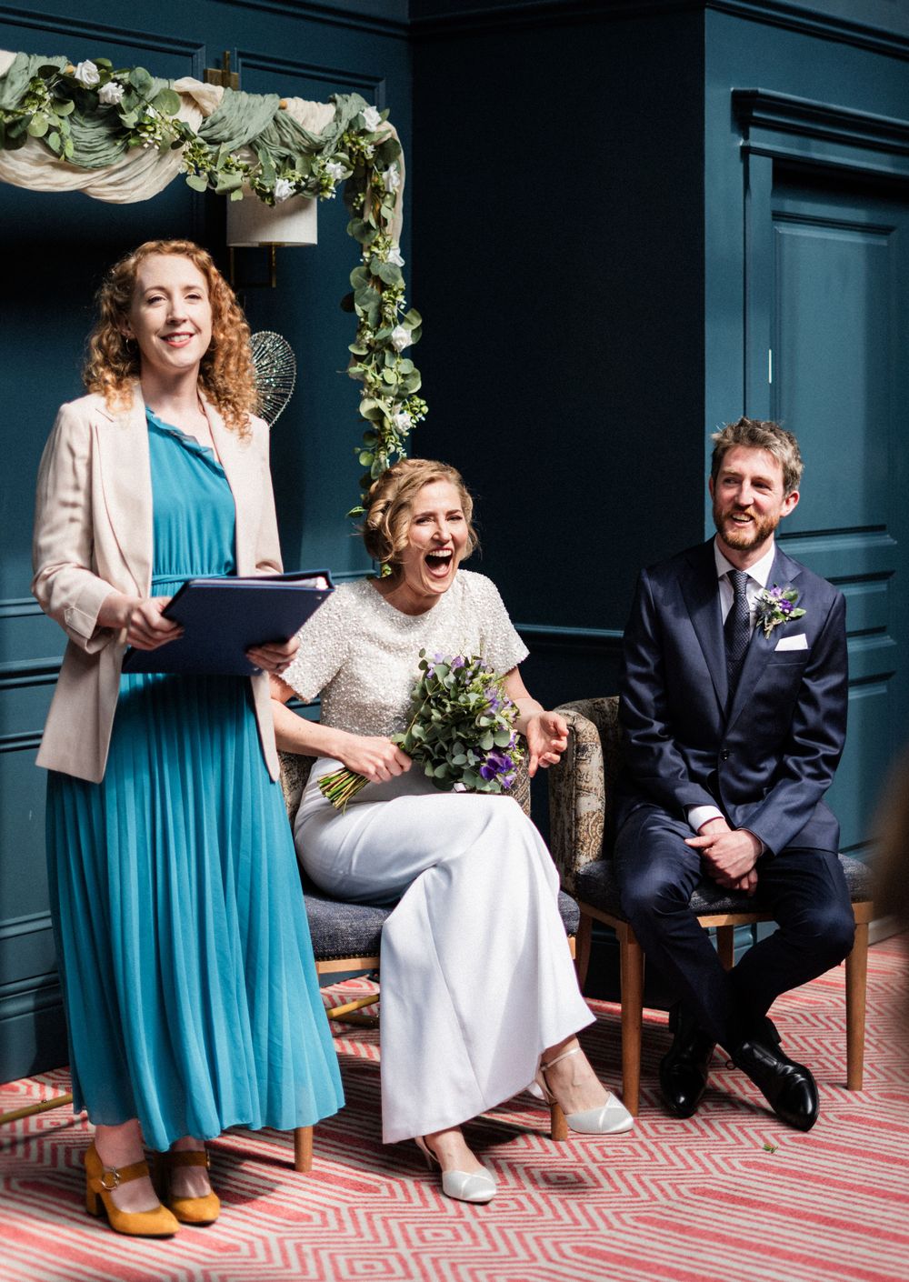 Wedding ceremony scene with floral arch and blue wall backdrop.