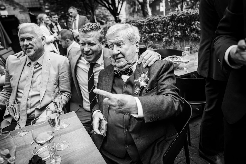 A black and white candid shot of wedding guests engaged in lively conversation.