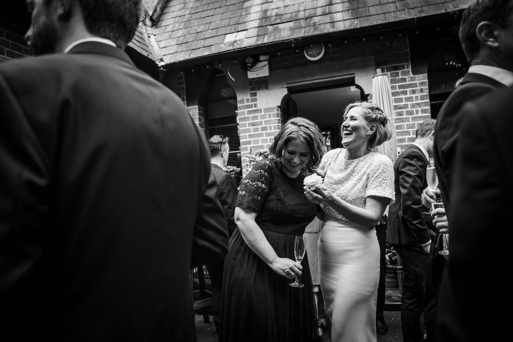 A black and white photograph capturing candid moments during an outdoor wedding reception.