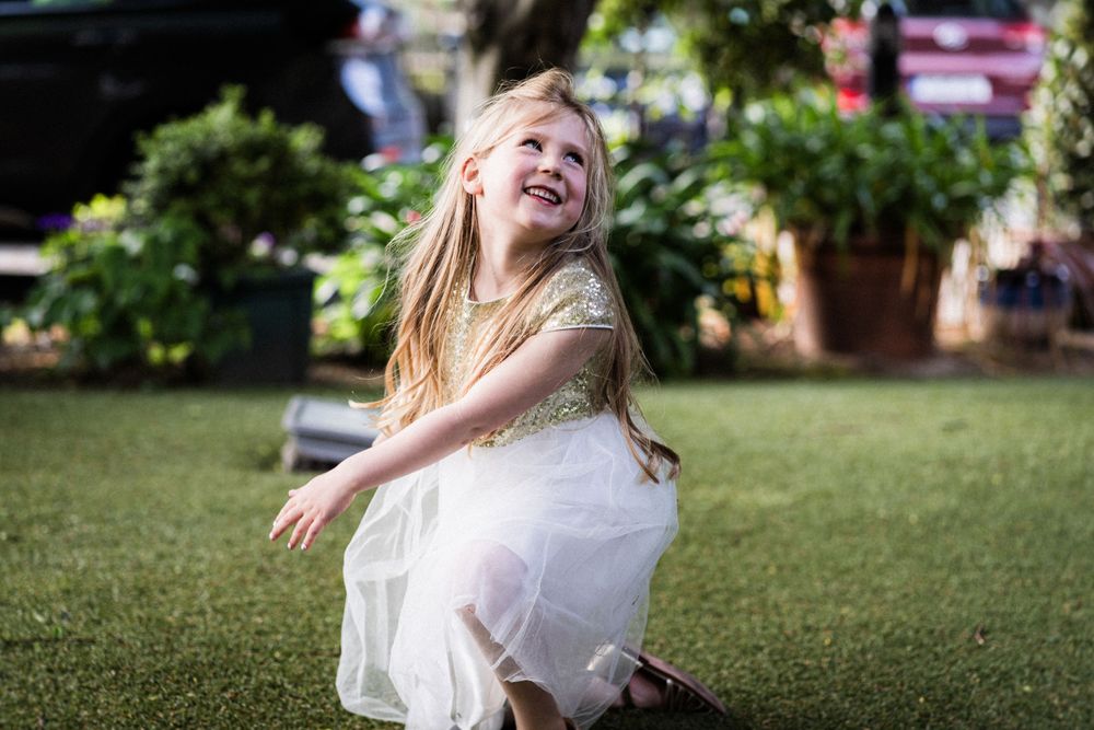 A young attendee in white twirls playfully on the lawn during the wedding celebration.