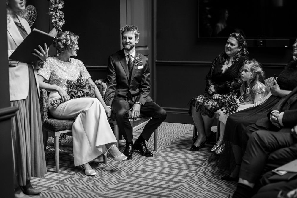 A black and white wedding photo showing guests seated in an intimate indoor venue with vintage decor.