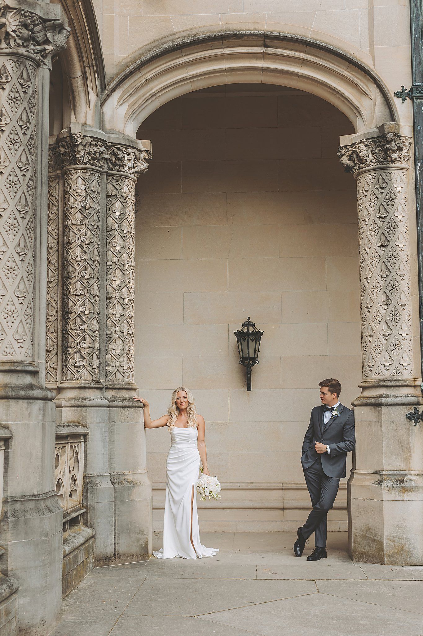 Classic wedding pose under decorative stone archway with vintage lantern detail.