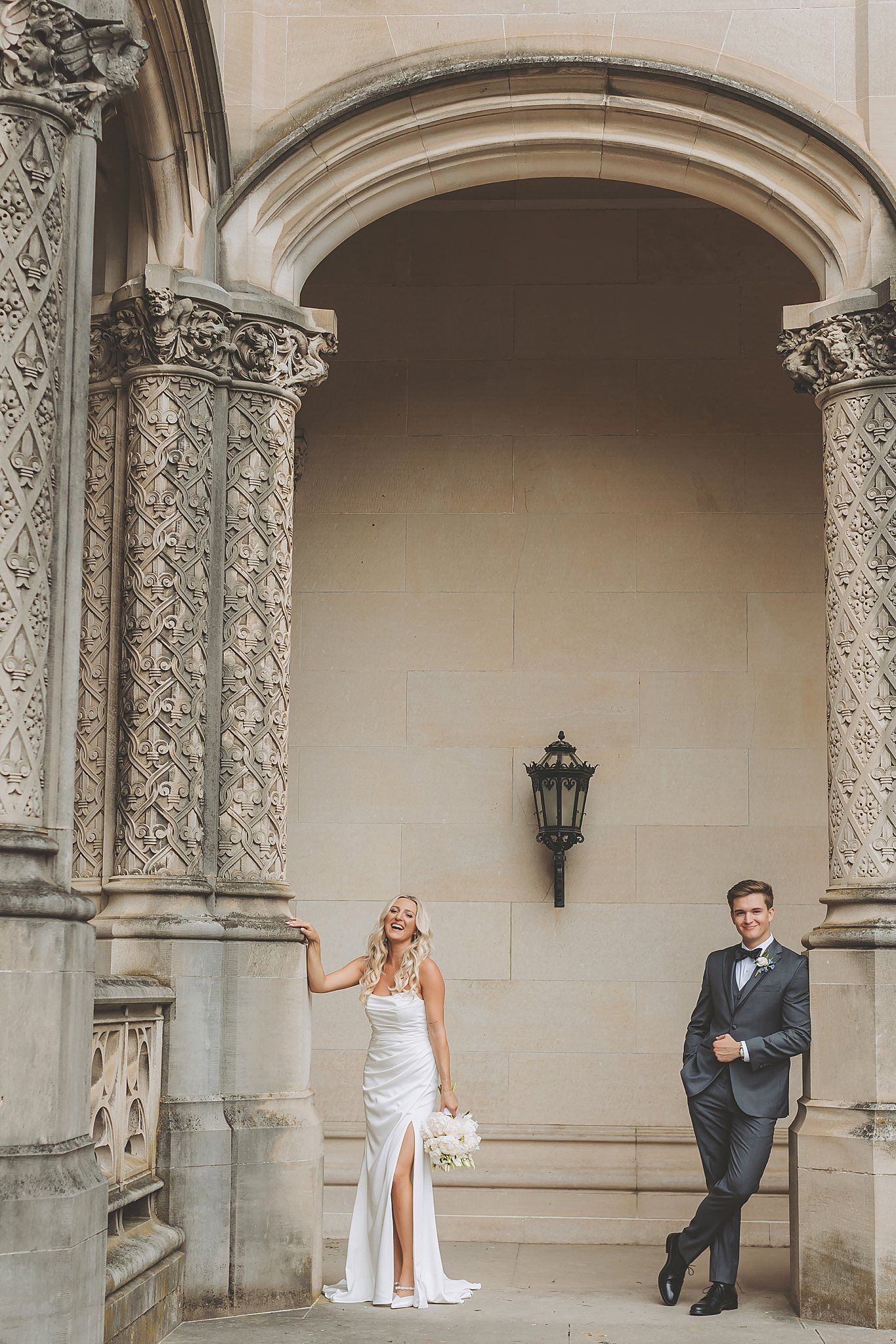 Elegant architectural wedding portrait beneath ornate stone archway with dramatic lighting.