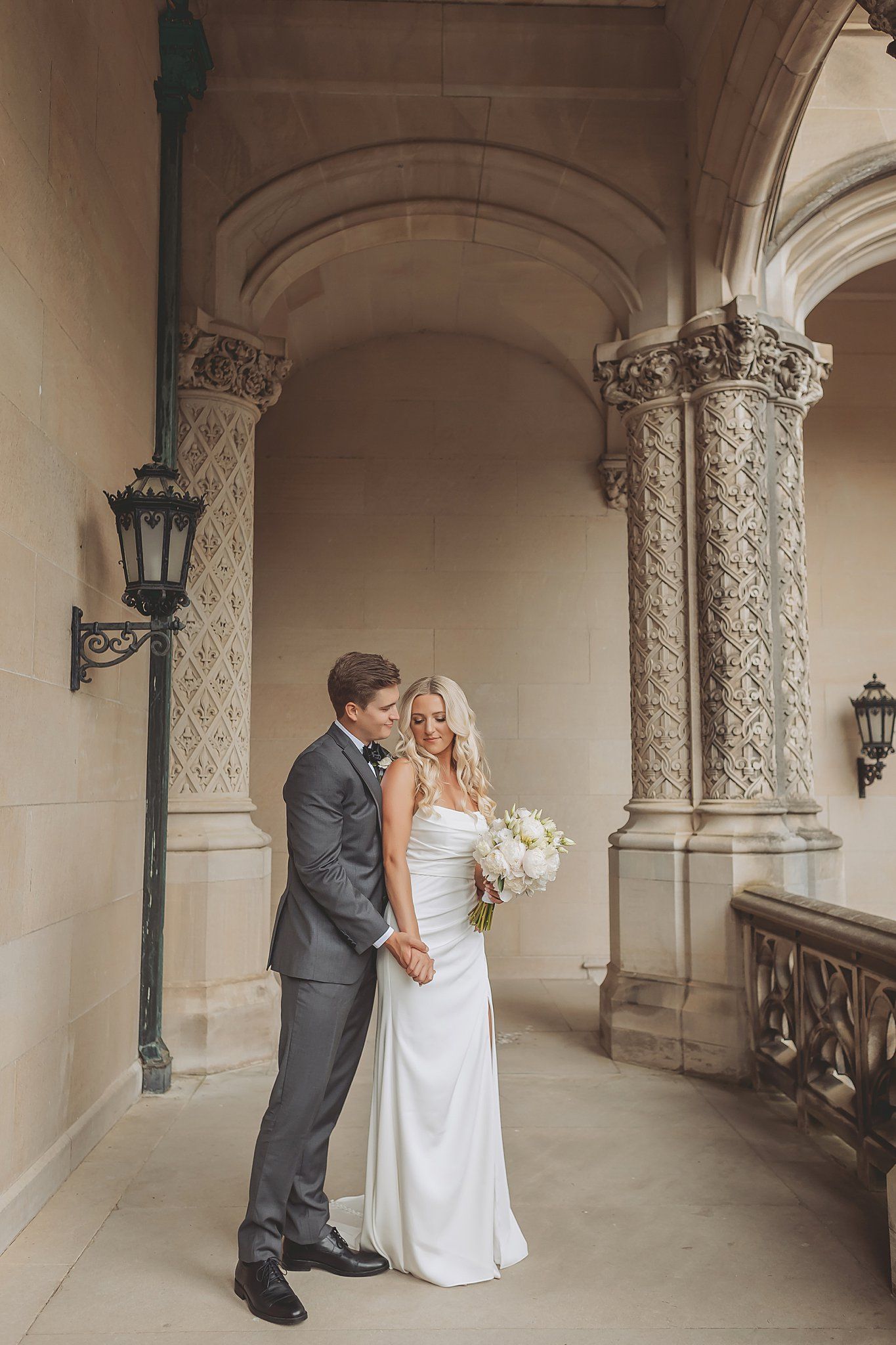 Wedding couple poses in a beautiful stone corridor with decorative columns and arches.
