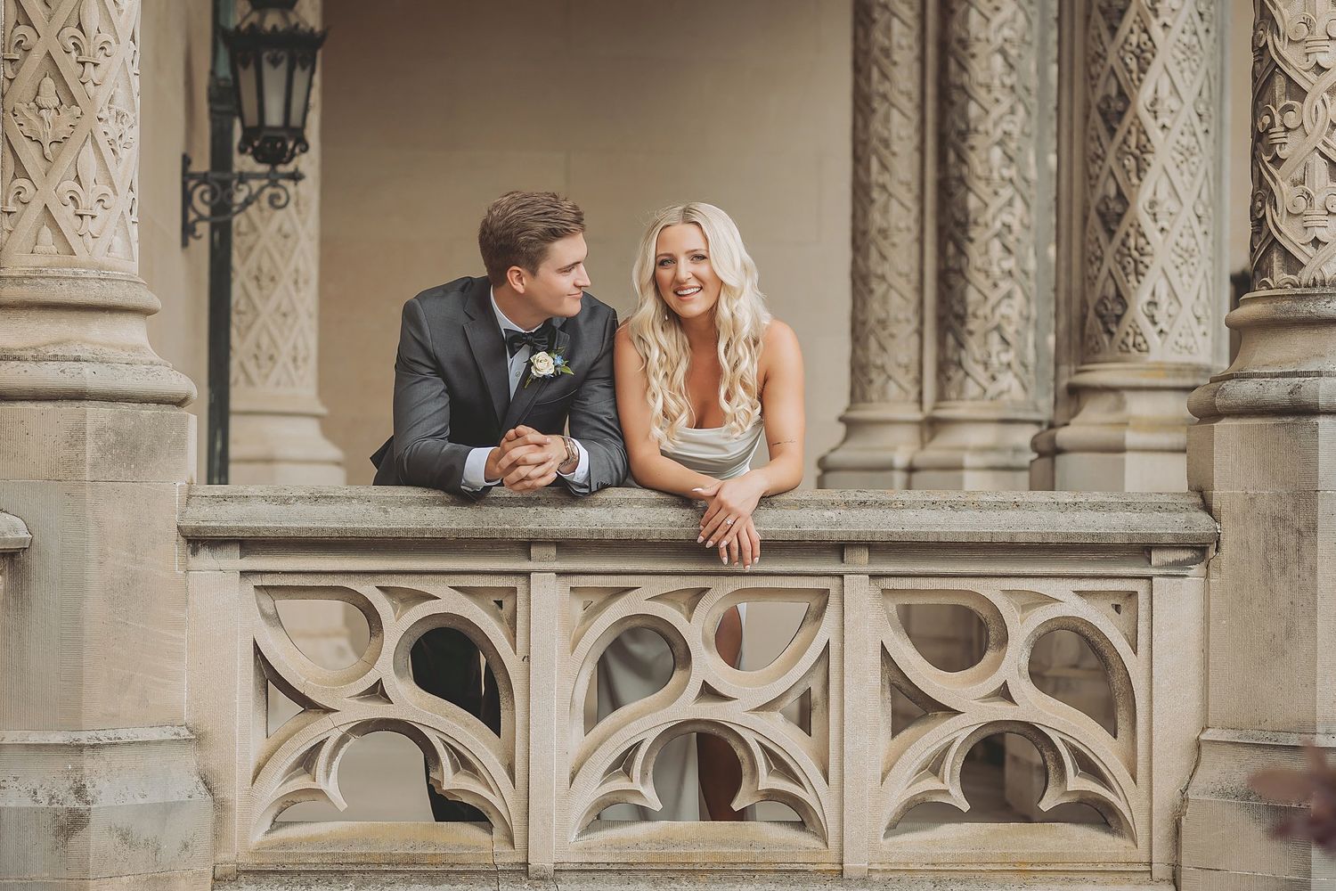 Newlywed couple sharing intimate moments in an elegant stone colonnade with gothic architectural details.