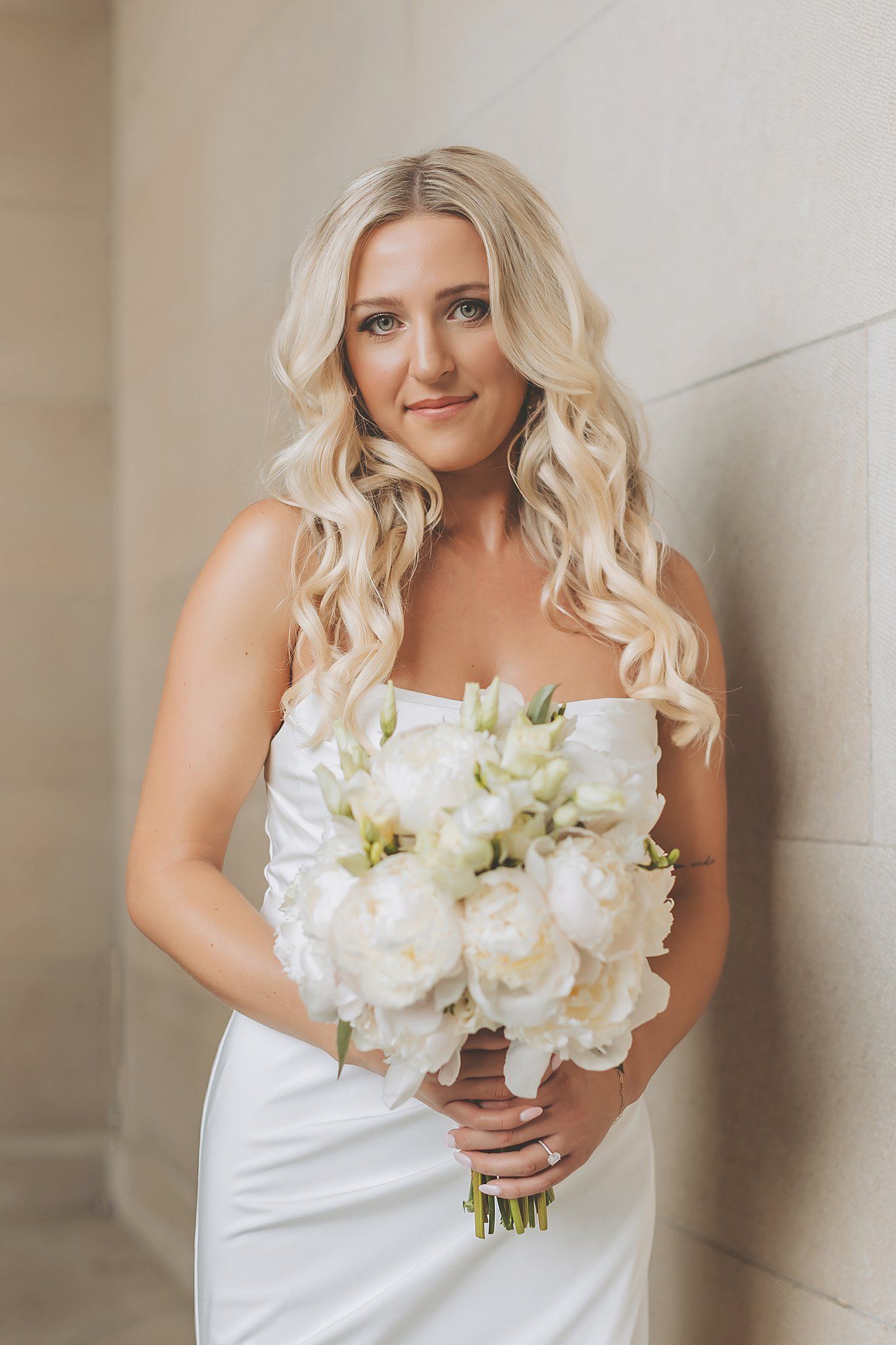 Beautiful bridal portraits with white bouquet against neutral stone background.