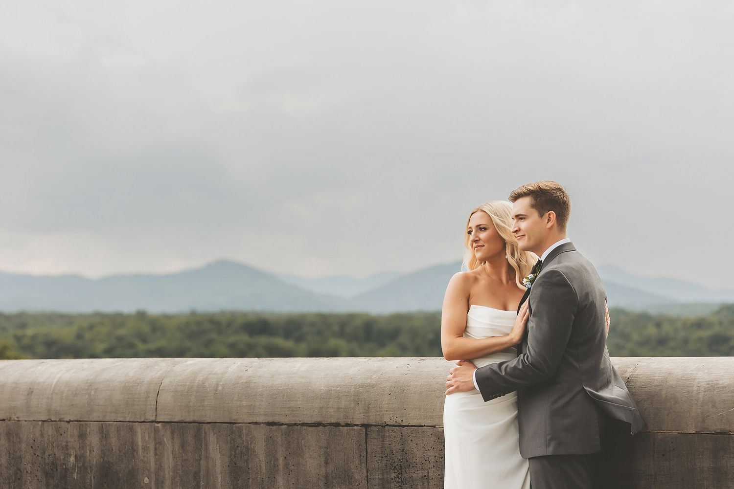 Couple shares intimate moment overlooking mountain vista from stone overlook.