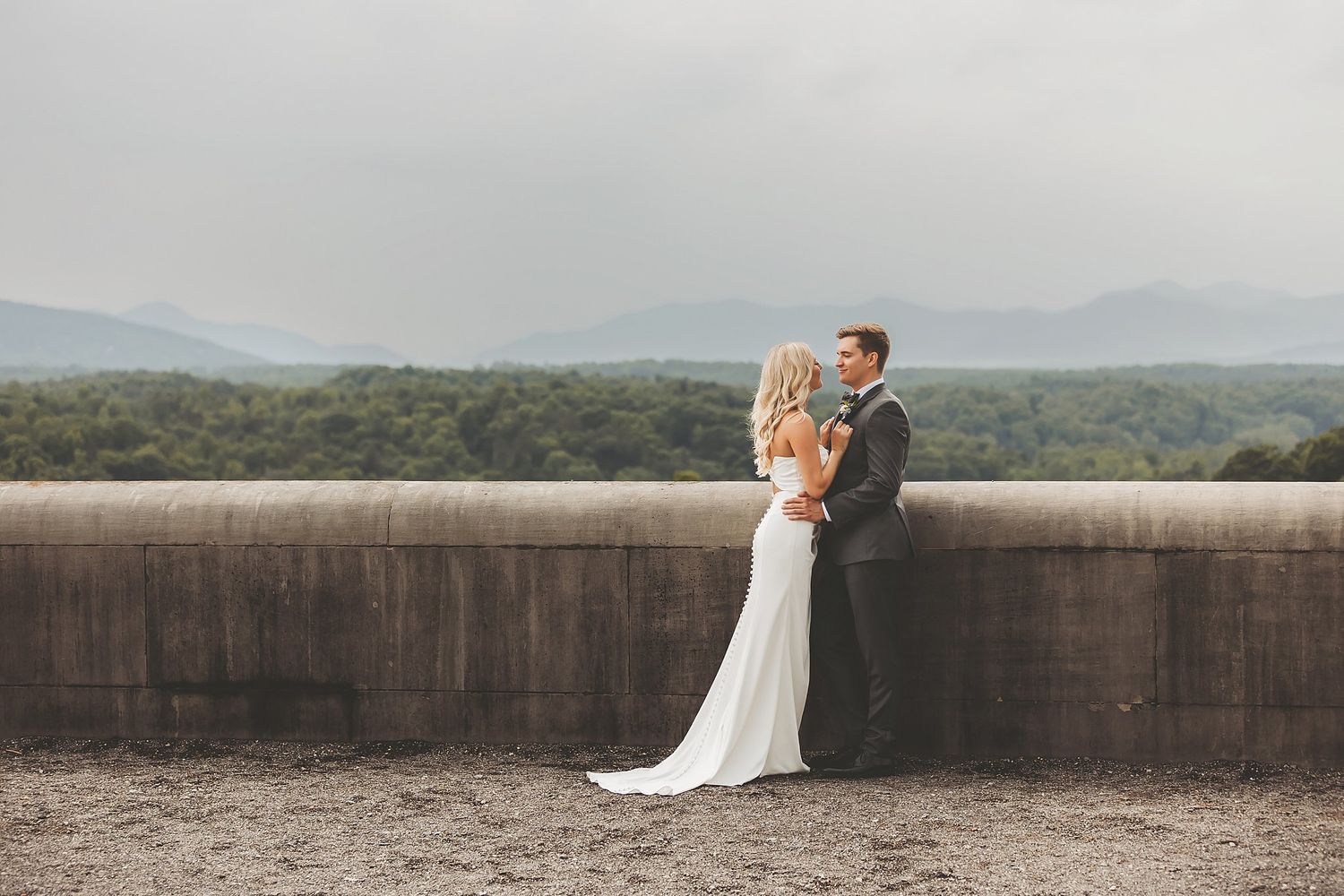 Newlyweds embrace against scenic mountain backdrop on stone terrace.