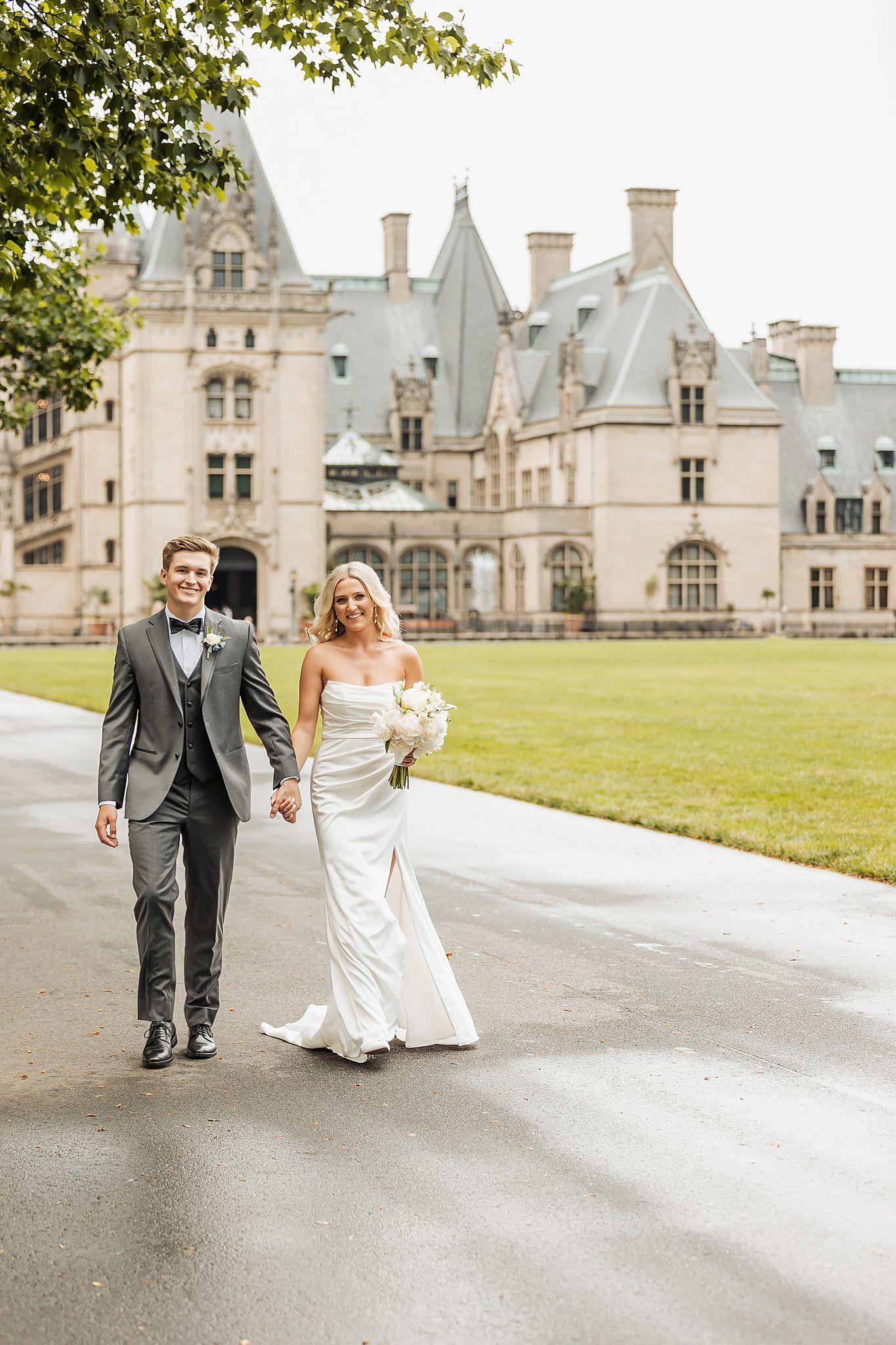 Couple walks along path with majestic Biltmore Estate castle in background.