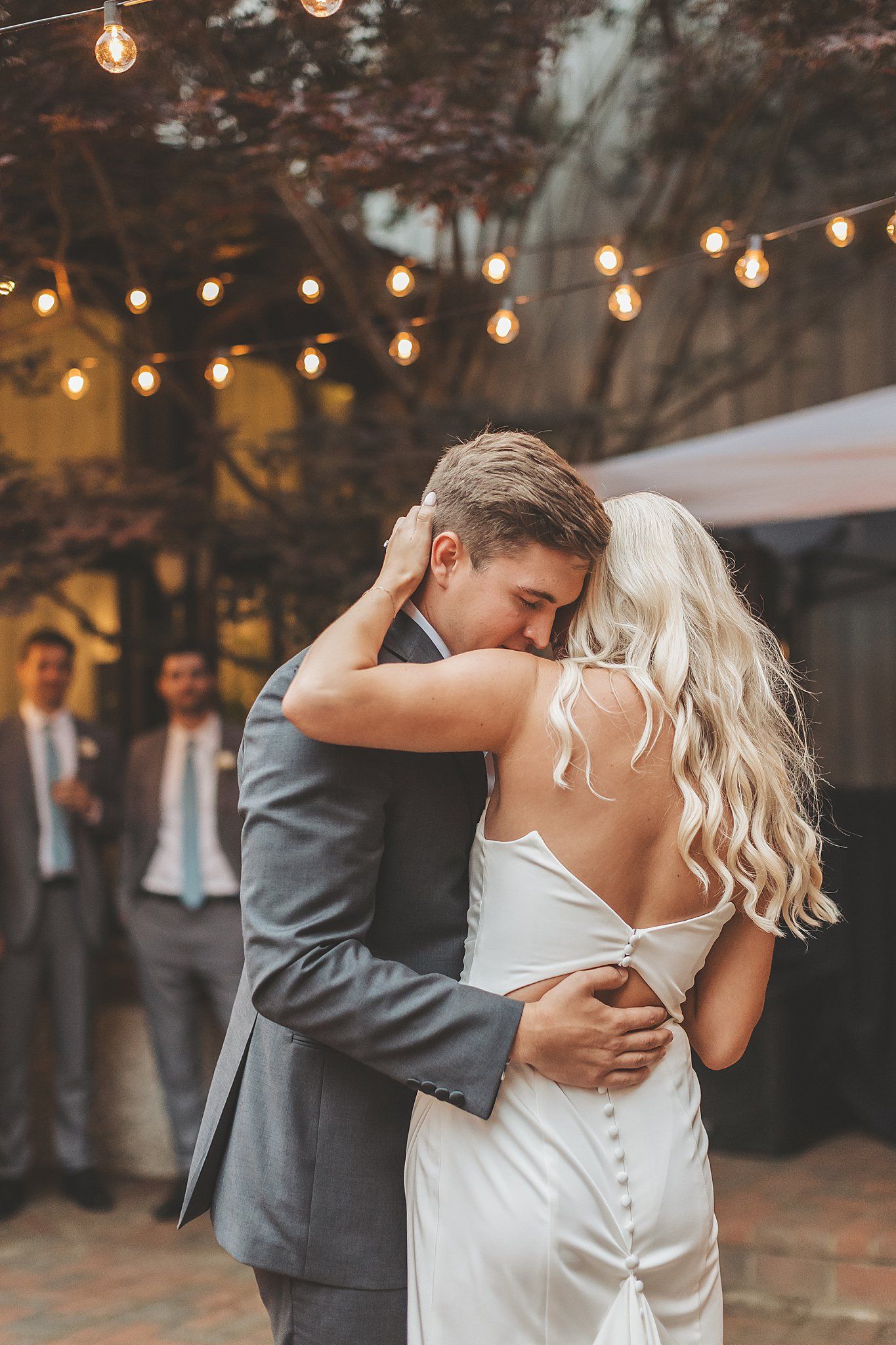 Intimate first dance moment under string lights at outdoor reception.