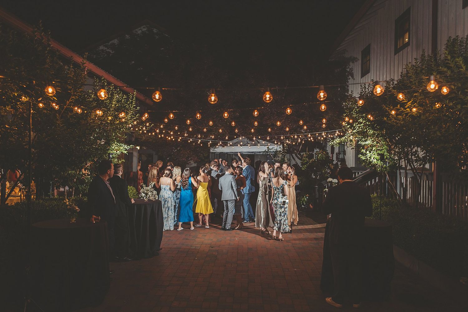 String lights illuminate an elegant outdoor evening wedding reception space.