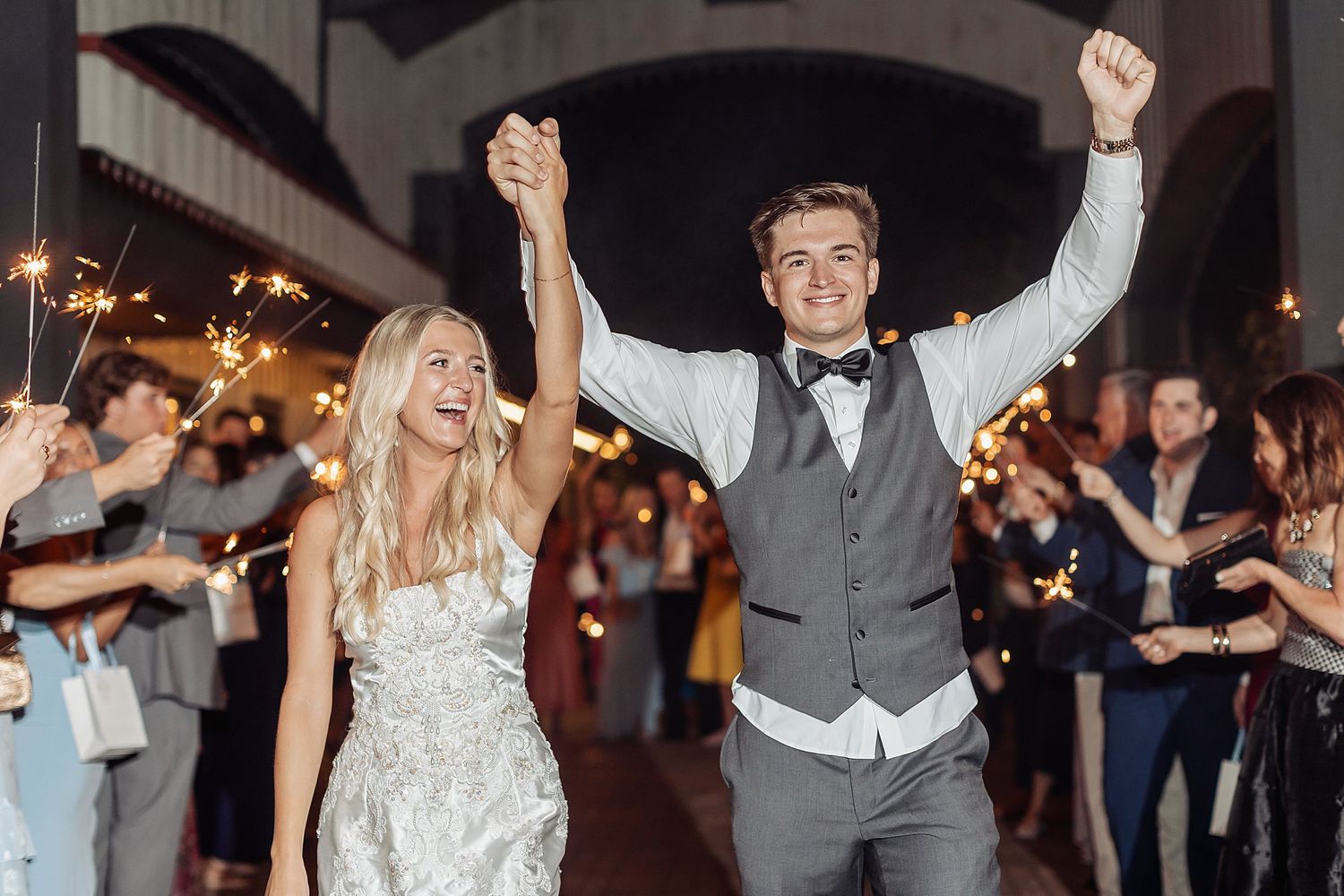 Joyful wedding guests raise their hands while dancing at night reception.