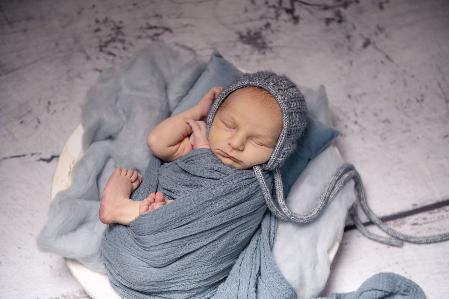 Peaceful newborn photography session with soft grey wrapping and minimal styling.