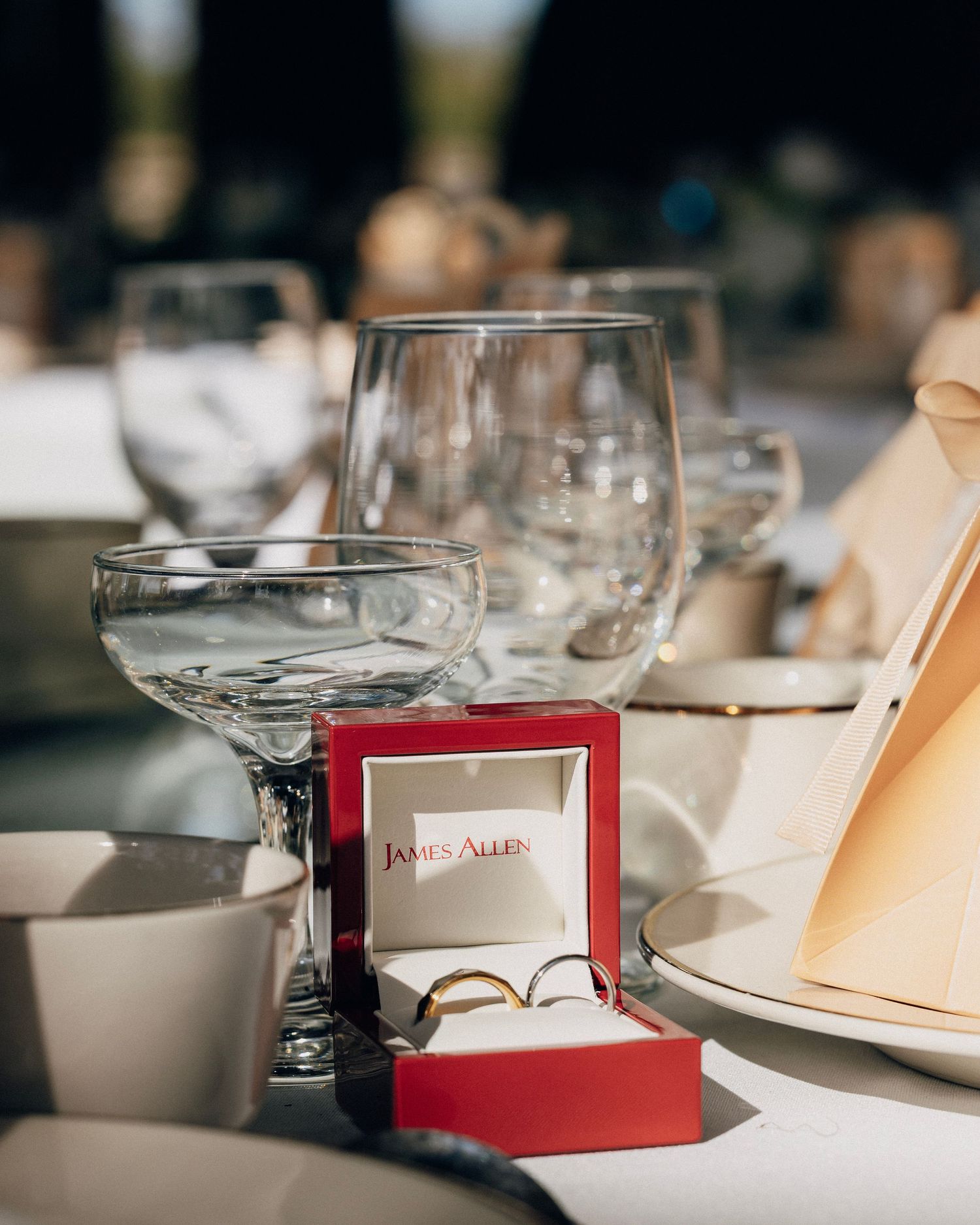 James Allen wedding rings displayed in a red box on an elegant outdoor reception table with crystal glassware.