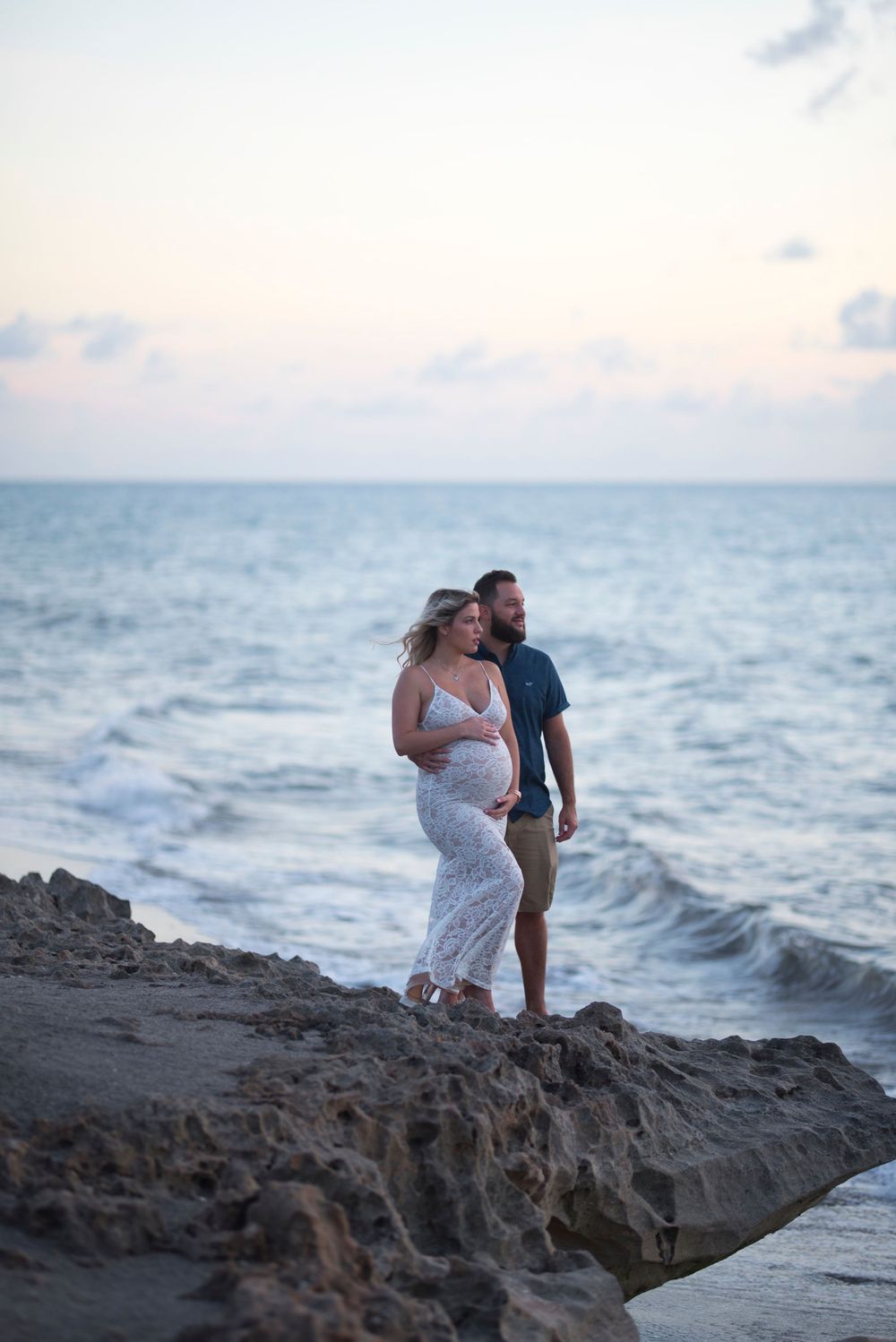 Romantic coastal photoshoot at sunset with rocky ocean backdrop.