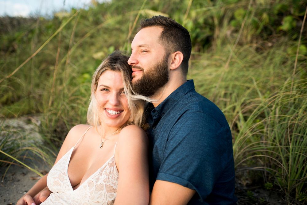 A romantic couple portrait in casual attire against a backdrop of coastal vegetation.
