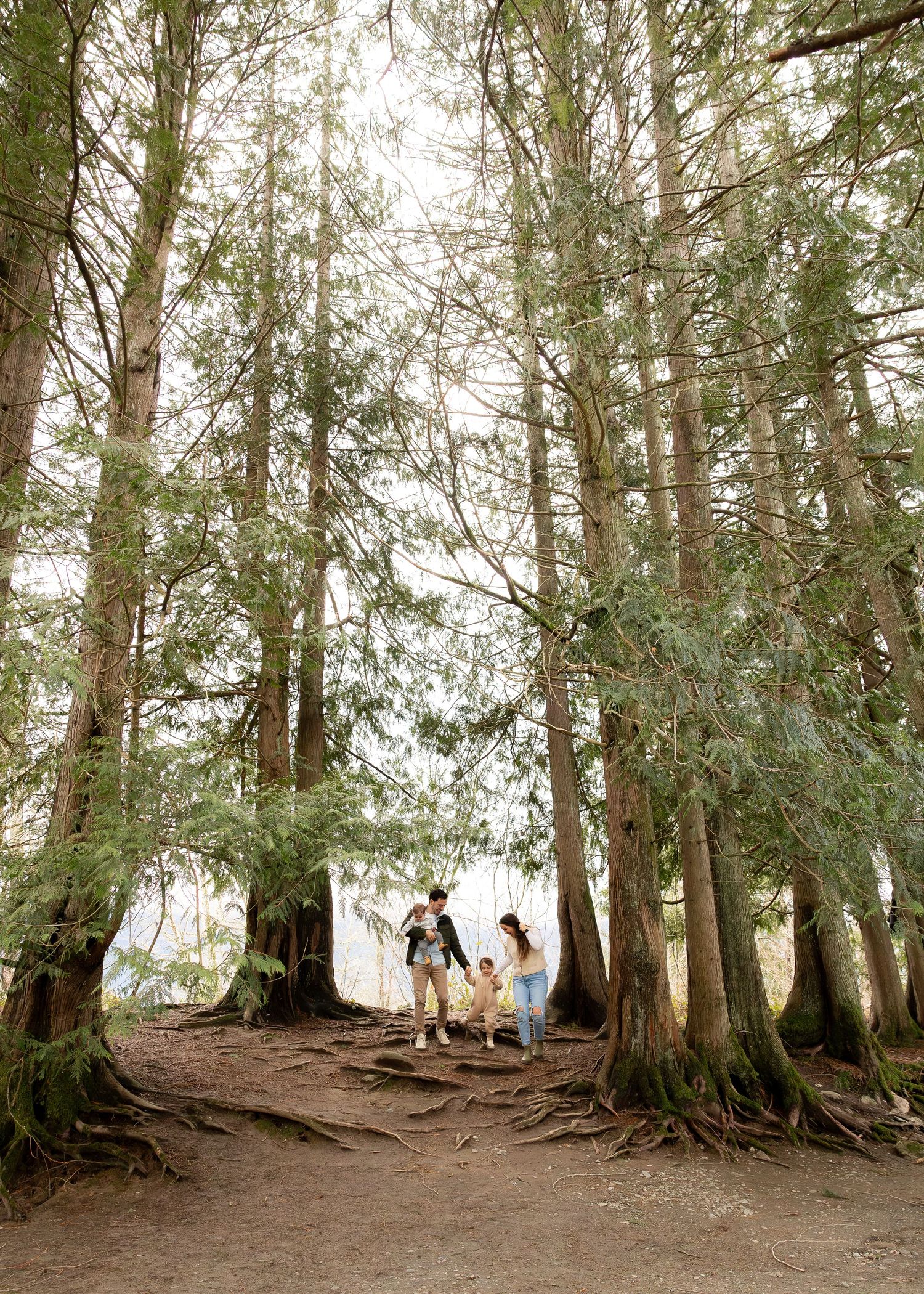 Family posing against white backdrop outdoors between trees in natural setting.