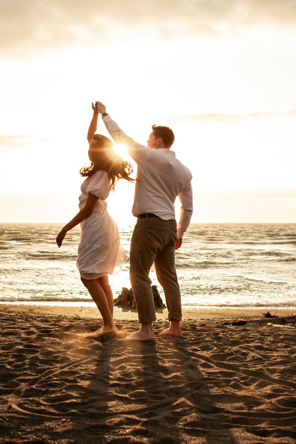 Silhouetted figures dance joyfully together on a sandy beach at sunset with golden light streaming through the scene.
