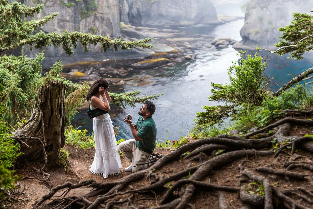 A couple poses together during an engagement photoshoot along a misty cliffside overlooking the ocean.