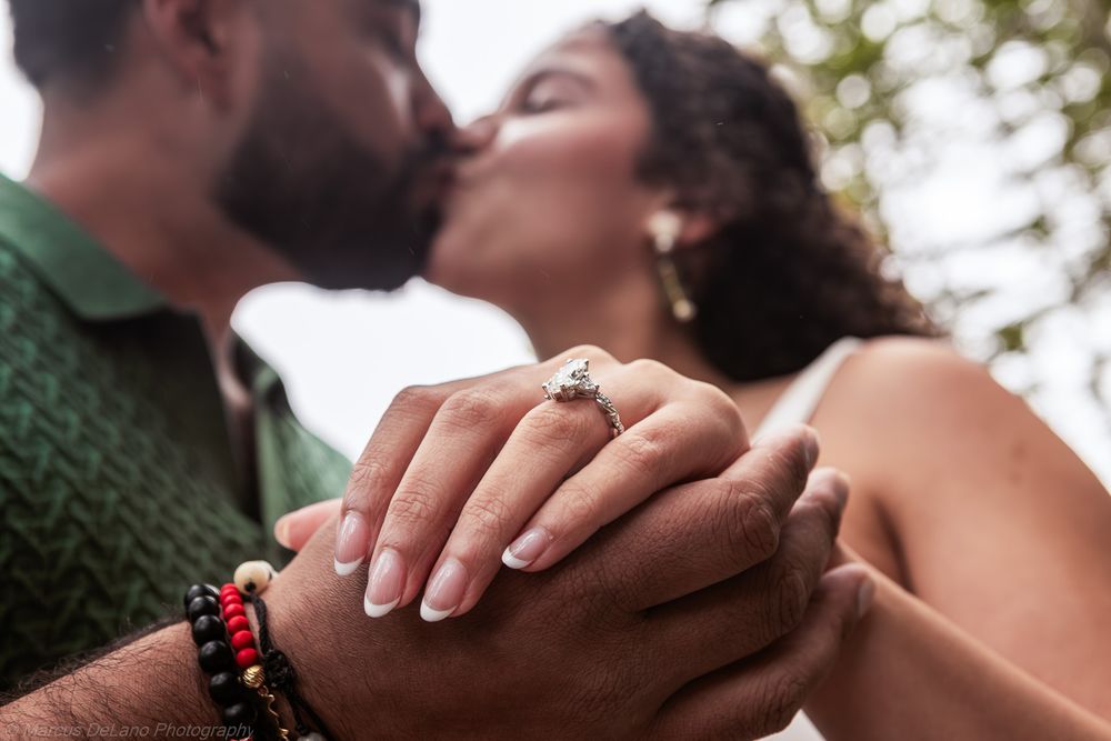 Close up of two hands with wedding rings touching against a blurred outdoor background.