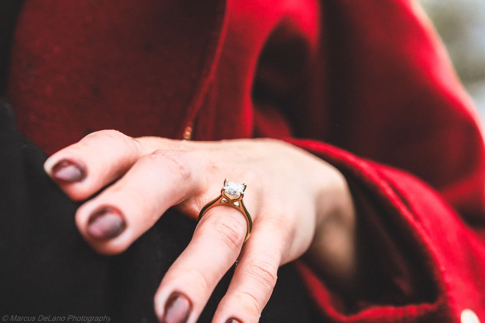 A close-up shot of hands wearing engagement rings against a red velvet background.