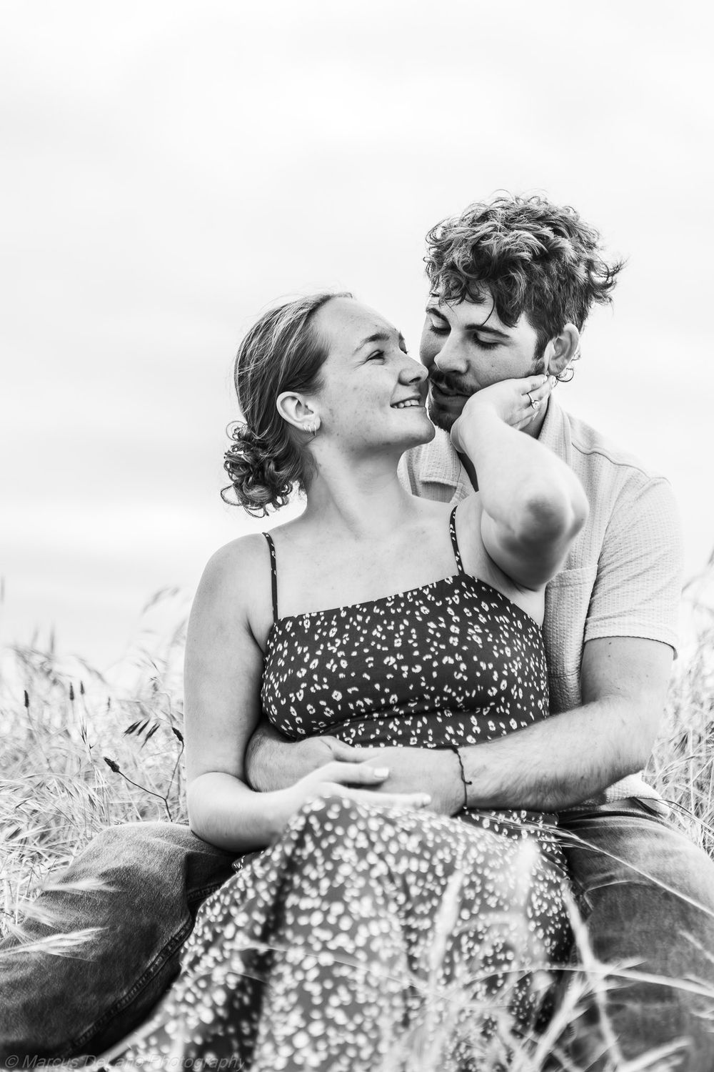 A couple lying together in a grassy field share intimate moments in a series of black and white photos.