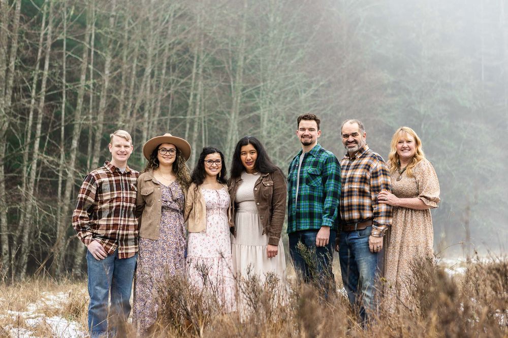 A group in coordinating plaid and floral outfits poses together in a misty field during autumn.