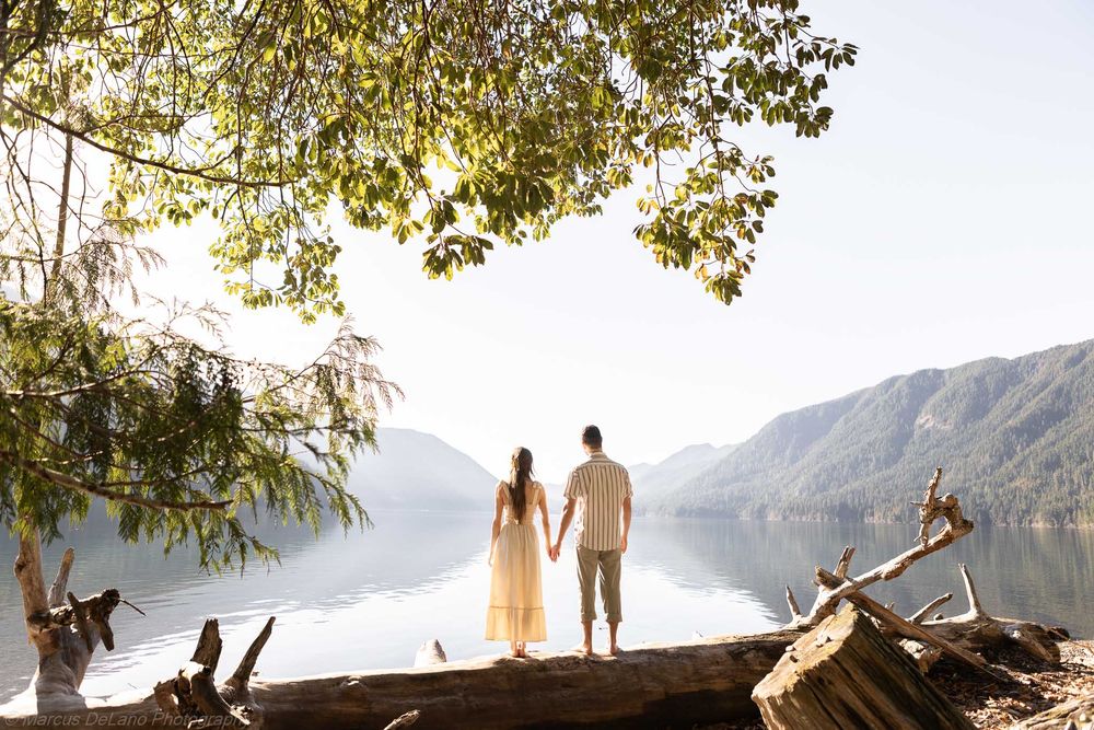 Couple stands on mountain overlook at sunset with scenic lake and mountain vista in background.