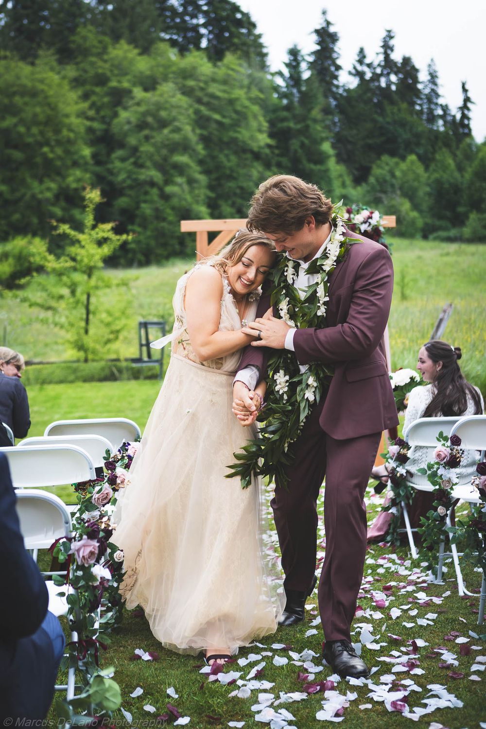 Bride and groom share an intimate moment at outdoor wedding ceremony, wearing floral garland, surrounded by rose petals.