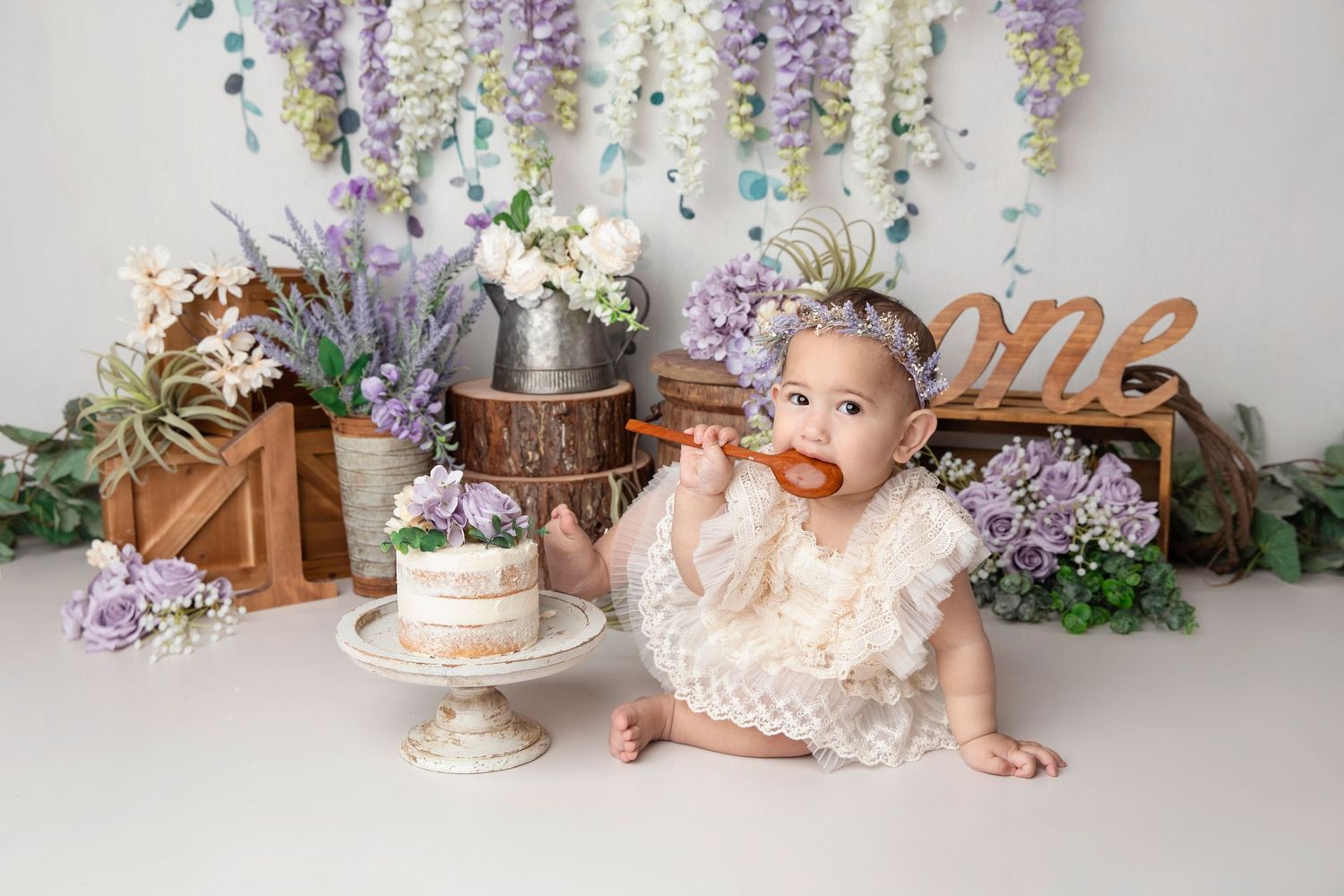 Floral backdrop with wisteria and cake setup for vintage style baby photography.