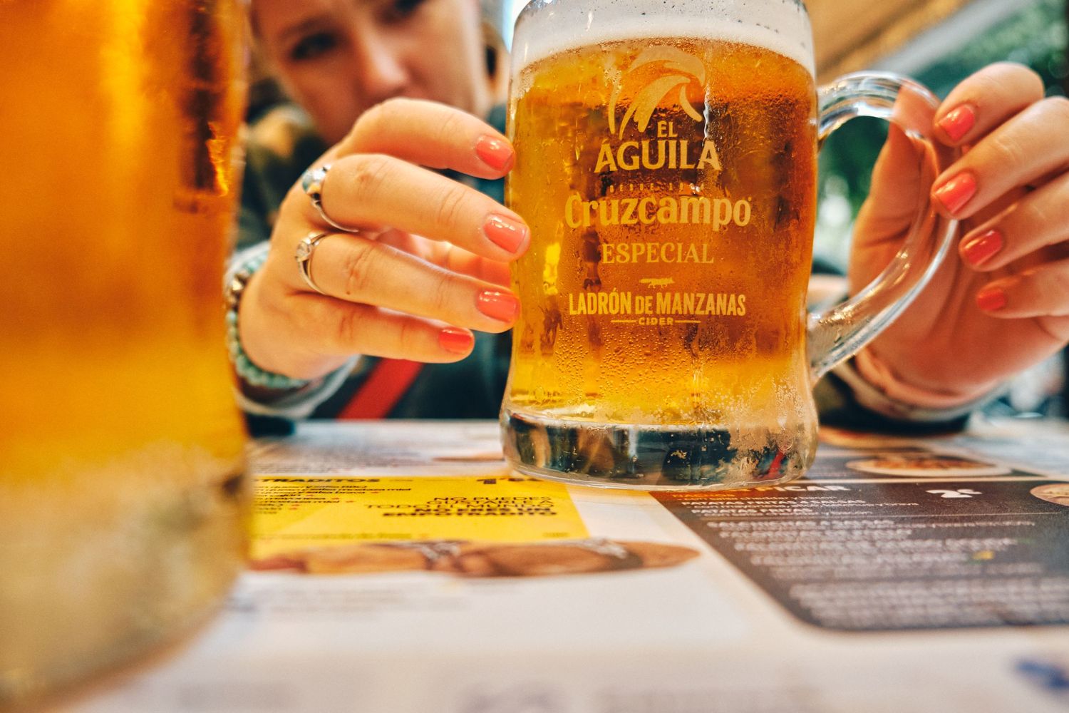 Close-up of a glass of golden Aguila Cruzcampo beer with menu in the background.