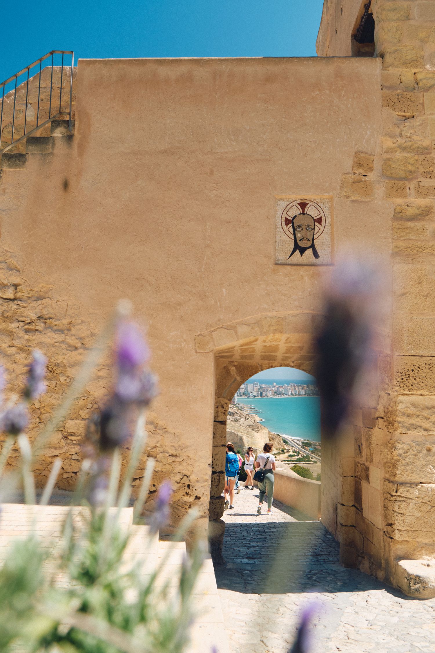 Stone archway with purple lavender flowers framing a view of the Mediterranean coast.
