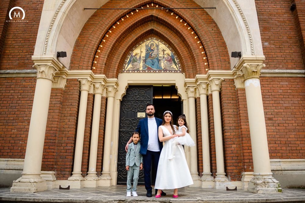 A family stands together under an ornate Gothic church doorway with cream columns and brick walls.
