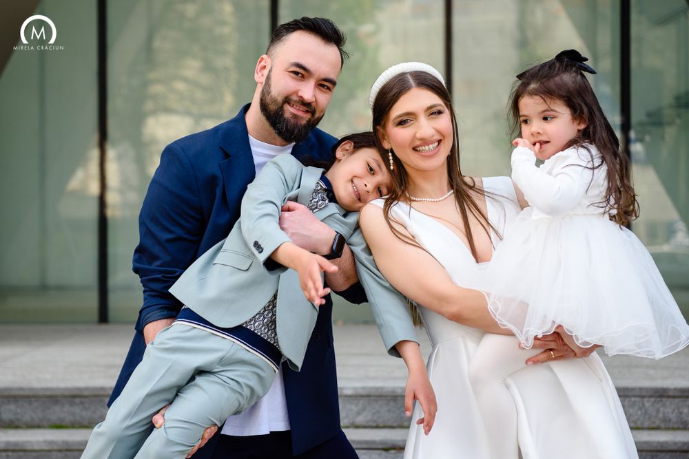 Modern family portrait showing parents and children dressed in elegant attire against glass building facade.