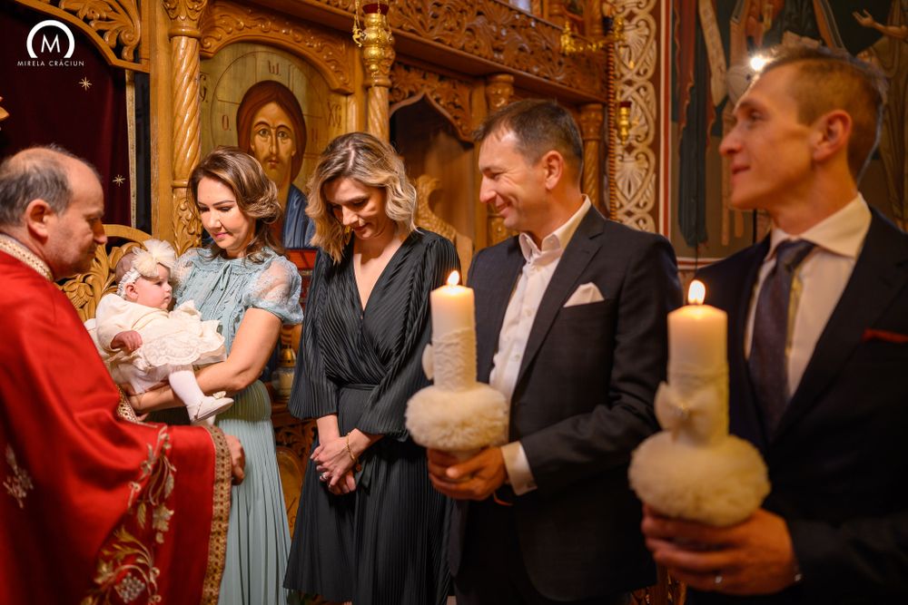 Traditional Orthodox baptism ceremony with religious officials and family members holding candles.