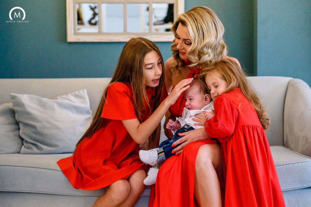 Family cuddles together on gray couch wearing matching red dresses.