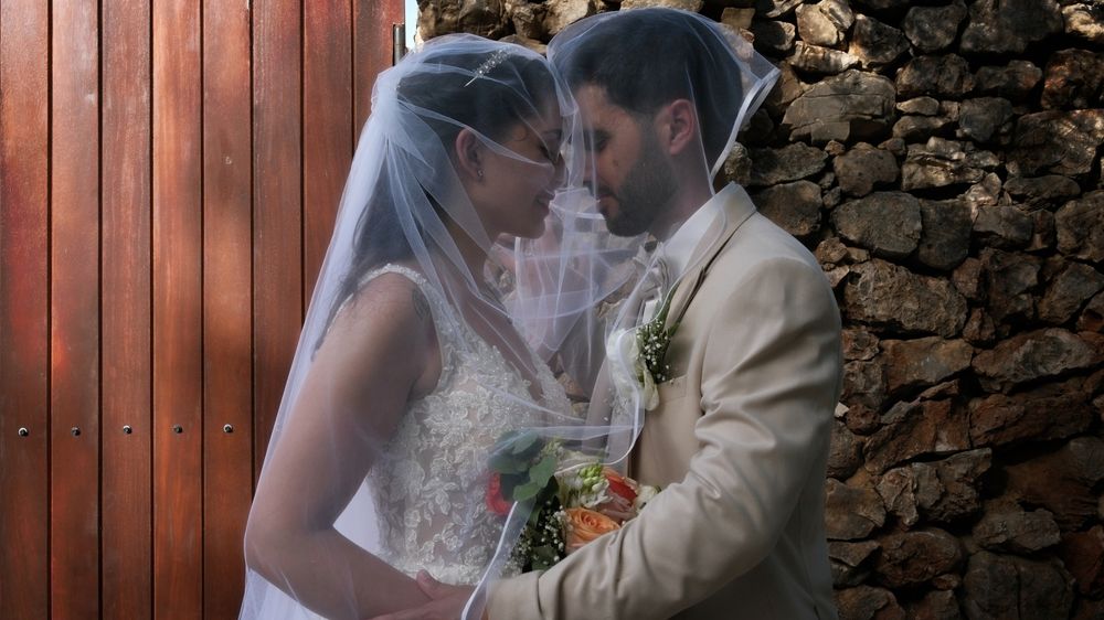 Bride and groom looking at each other, covered by the bride's wedding veil during a newlyweds photo session.