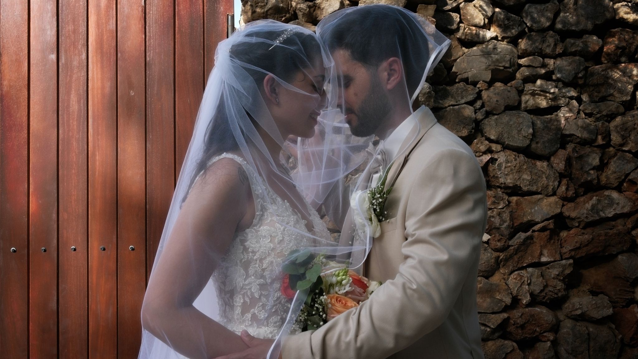 Bride and groom looking at each other, covered by the bride's wedding veil during a newlyweds photo session.