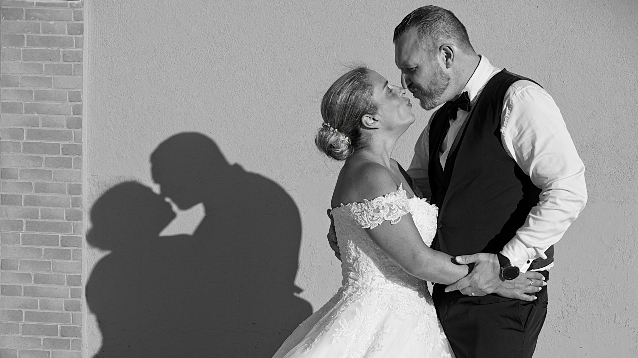 Bride and groom embracing beside a wall, with their kissing shadow reflected.