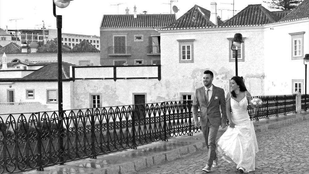 Black and white photograph of bride and groom walking hand in hand on the Roman Bridge in Tavira.
