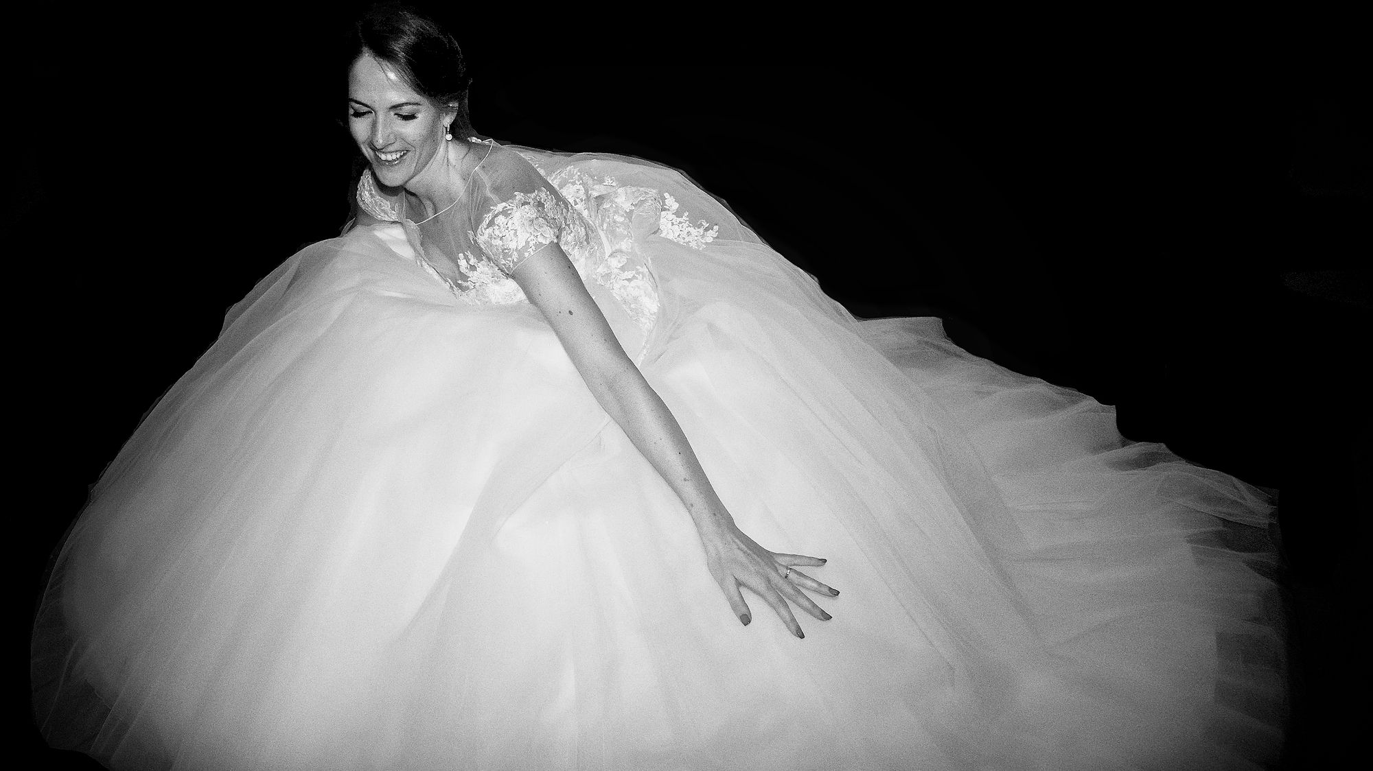 High contrast black and white photo of a bride in a voluminous ball gown wedding dress with delicate lace details.