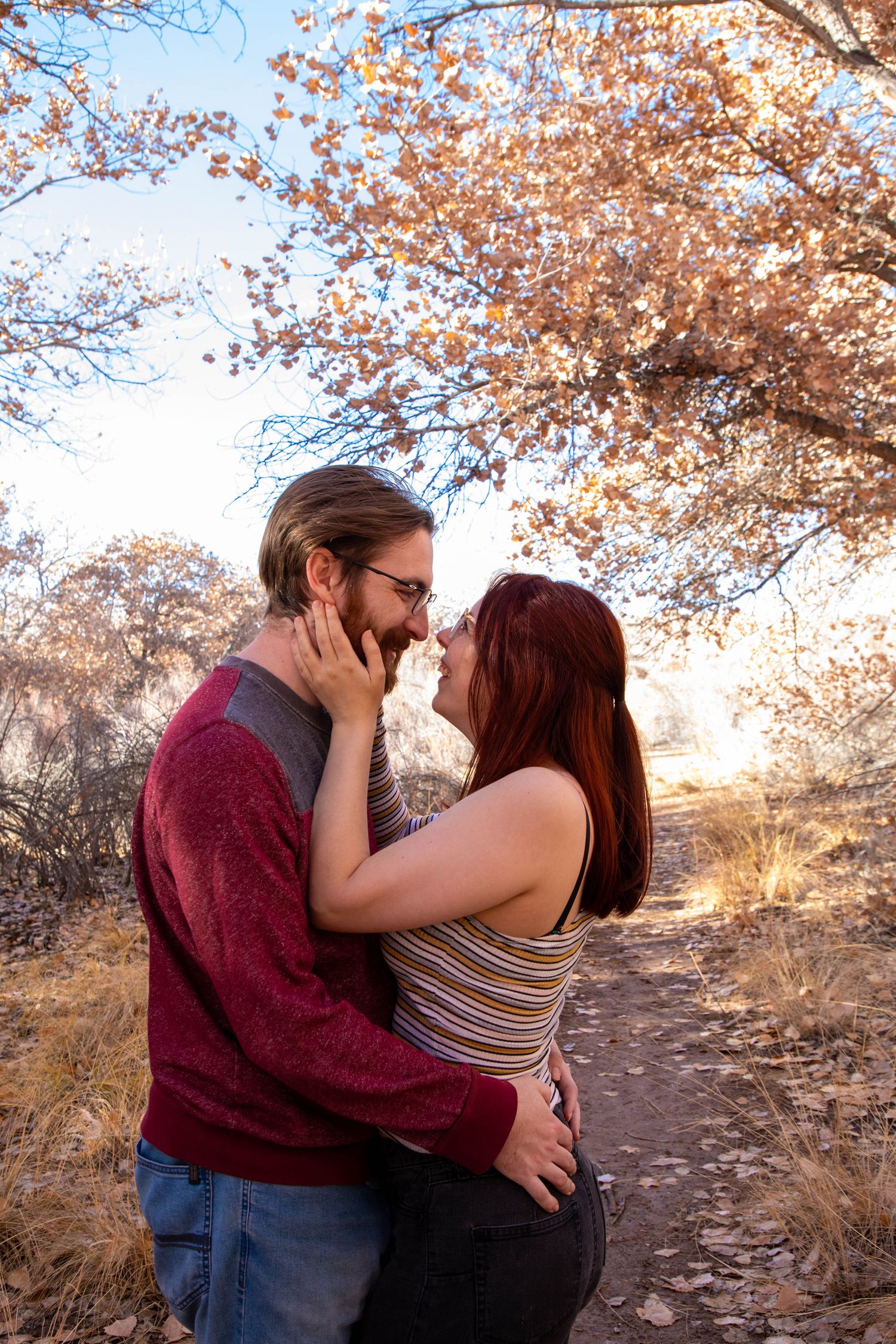 Romantic couple embracing under autumn trees with sunlight filtering through branches.
