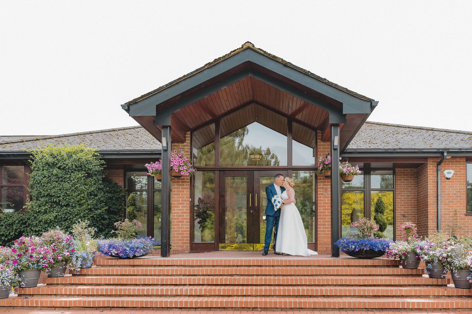 A modern wedding venue exterior with brick steps, blue flowers, and glass windows.
