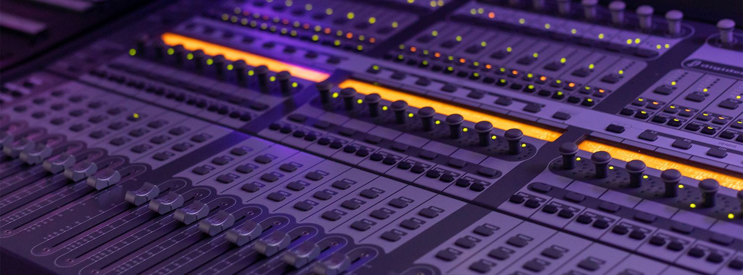Close up of a professional audio mixing console with illuminated faders and controls in purple lighting.
