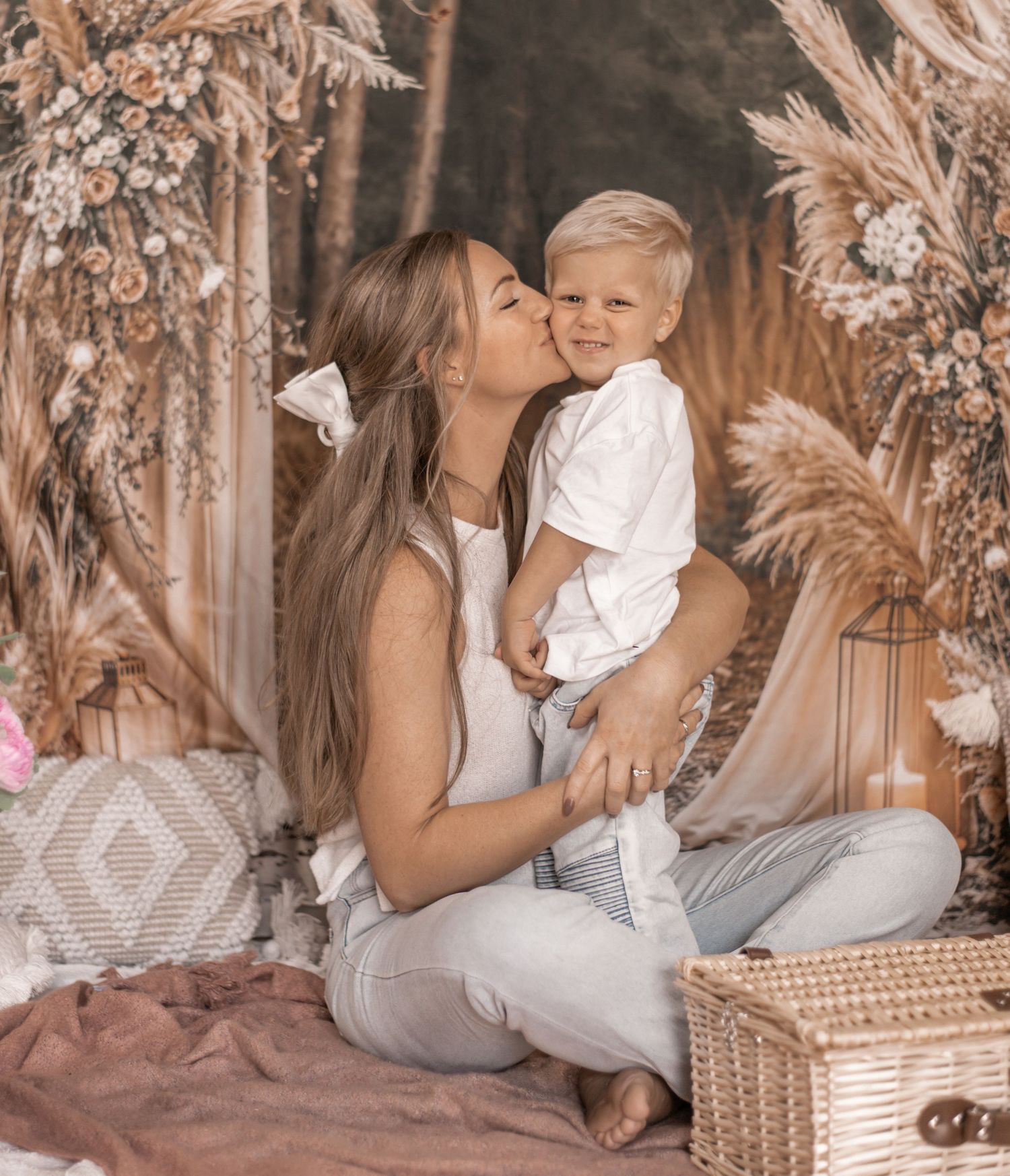 Mother and baby sharing an intimate moment on a decorative peacock chair with warm lighting and textured backdrop.