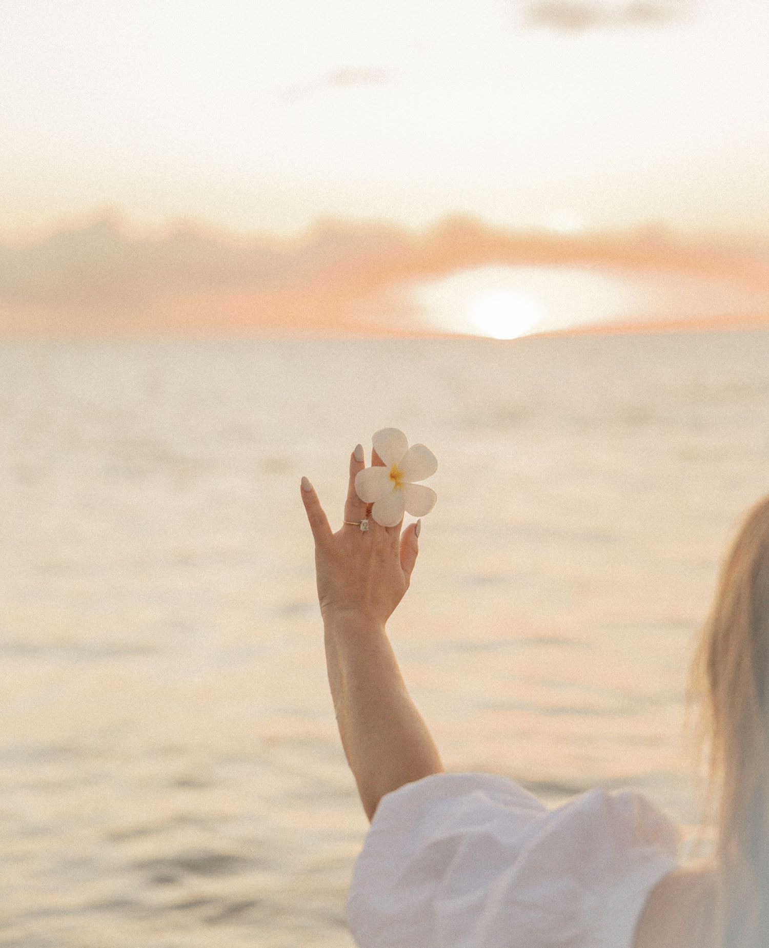 Hand raised against a dreamy sunset sky over calm ocean waters during golden hour.