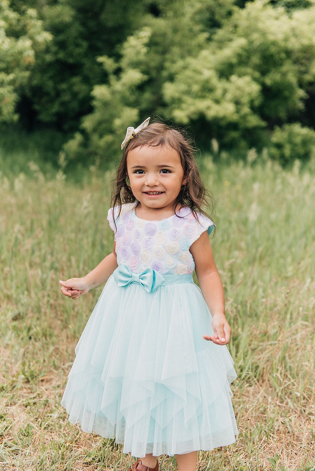 Young child in a mint tulle dress twirls in a sunlit meadow during summer.